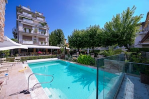 A swimming pool with a glass barrier, surrounded by lounge chairs and potted plants. - Il Bacco few Steps From sea (Camaiore)