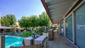 A poolside area with a table and chairs, a glass-enclosed patio, and a view of the pool. - Il Bacco few Steps From sea (Camaiore)