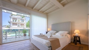 A bedroom with a large bed, a view of the outside balcony, and a small table with a lamp. - Il Bacco few Steps From sea (Camaiore)