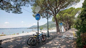 En asfalteret sti med parkerede cykler, en strand i baggrunden og en klar himmel.