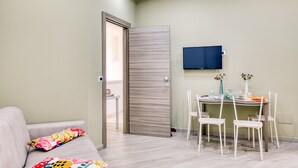 Un saló modern amb un sofà, una taula de menjador amb caires, un televisor penjat a la paret i una porta que dona a una altra habitació.