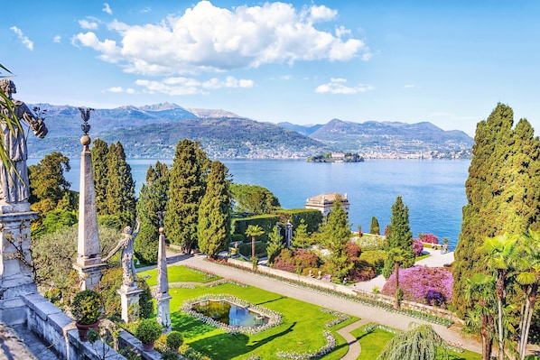 A formal garden with statues, a pond, and a view of a lake and mountains.