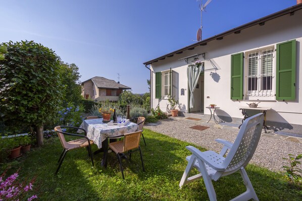 A patio with a table and chairs, surrounded by a garden with potted plants and a hedge. - La Casa Sul Lago Maggiore (Ranco)