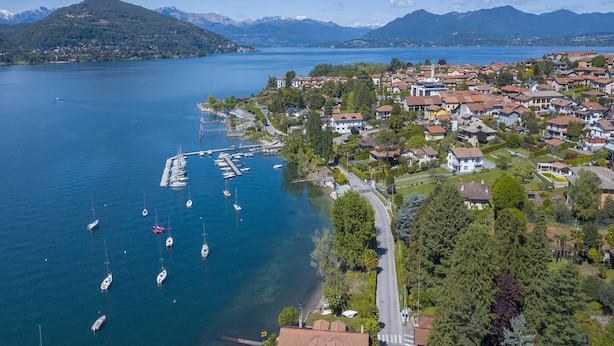 Luchtbeeld van een stad aan een meer, met woongebouwen, een jachthaven vol boten en bergen op de achtergrond.