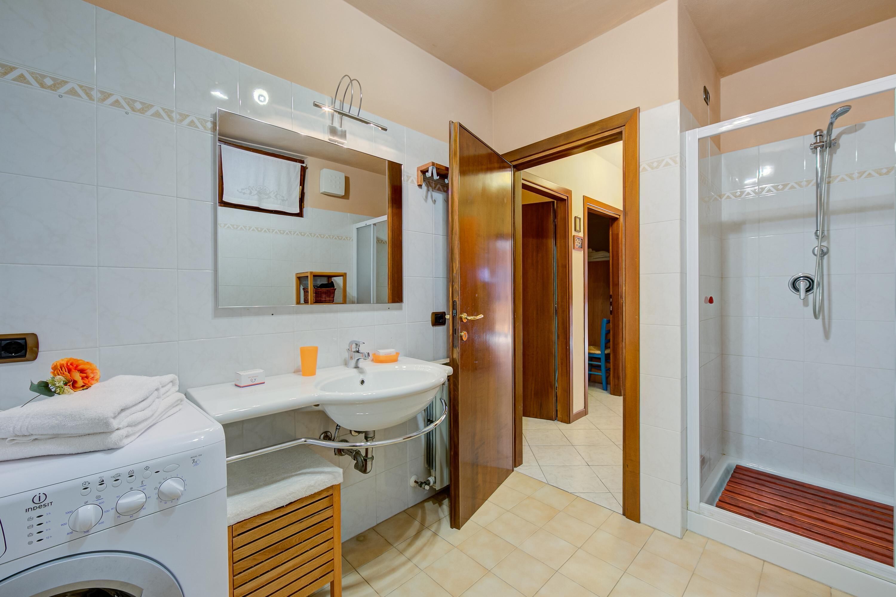A modern bathroom with a washing machine, a sink, a mirror, and a shower area.