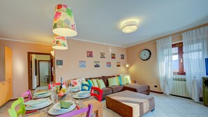 Uma sala de jantar com uma mesa posta para quatro pessoas, um sofá e um relógio na parede.