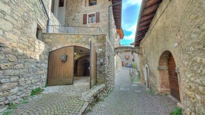 Une étroite ruelle pavée, bordée de bâtiments en pierre aux portes et volets en bois, qui mène à une cour intérieure.