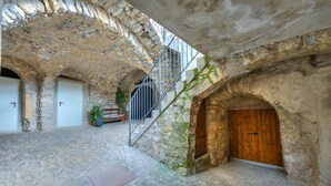 Μια πλακόστρωτη αυλή με μια σκάλα, μια ξύλινη πόρτα και ένα φυτό σε γλάστρα.