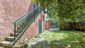 Una escalera conduce a un edificio con una puerta verde, rodeado de un jardín con césped y un sendero de piedra.