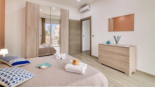 Ein modernes Schlafzimmer mit einem großen Bett, einem Schminktisch, einem Spiegel und einer Klimaanlage.