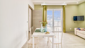 Ein modernes Wohnzimmer mit Essbereich, einem flachbildfernseher an der Wand und einem Balkon mit Blick.