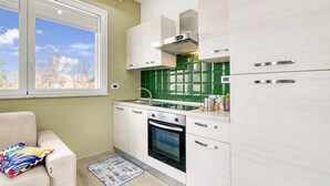 Eine kompakte Küche mit Fenster, einem Einbauofen und einer grünen Spritzschutzwand.