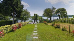 A pathway leading to a seating area by a lake, surrounded by lush greenery and trees. - Casa Maddalena Private Beach Upon Reques (Cadrezzate con Osmate)