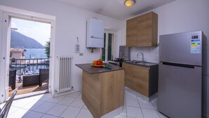 Une cuisine moderne avec un îlot central en bois, un réfrigérateur Samsung et une vue sur la mer par une porte ouverte.
