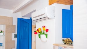 A room with a blue door, an air conditioning unit, a wall-mounted flower vase with tulips, and a tiled counter with a decorative plate. - Casa Demetra 200m From sea (Syracuse)