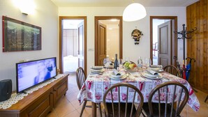 Un coin repas avec une table dressée pour quatre personnes, un téléviseur posé sur un meuble en bois et un porte-manteau avec des parapluies.
