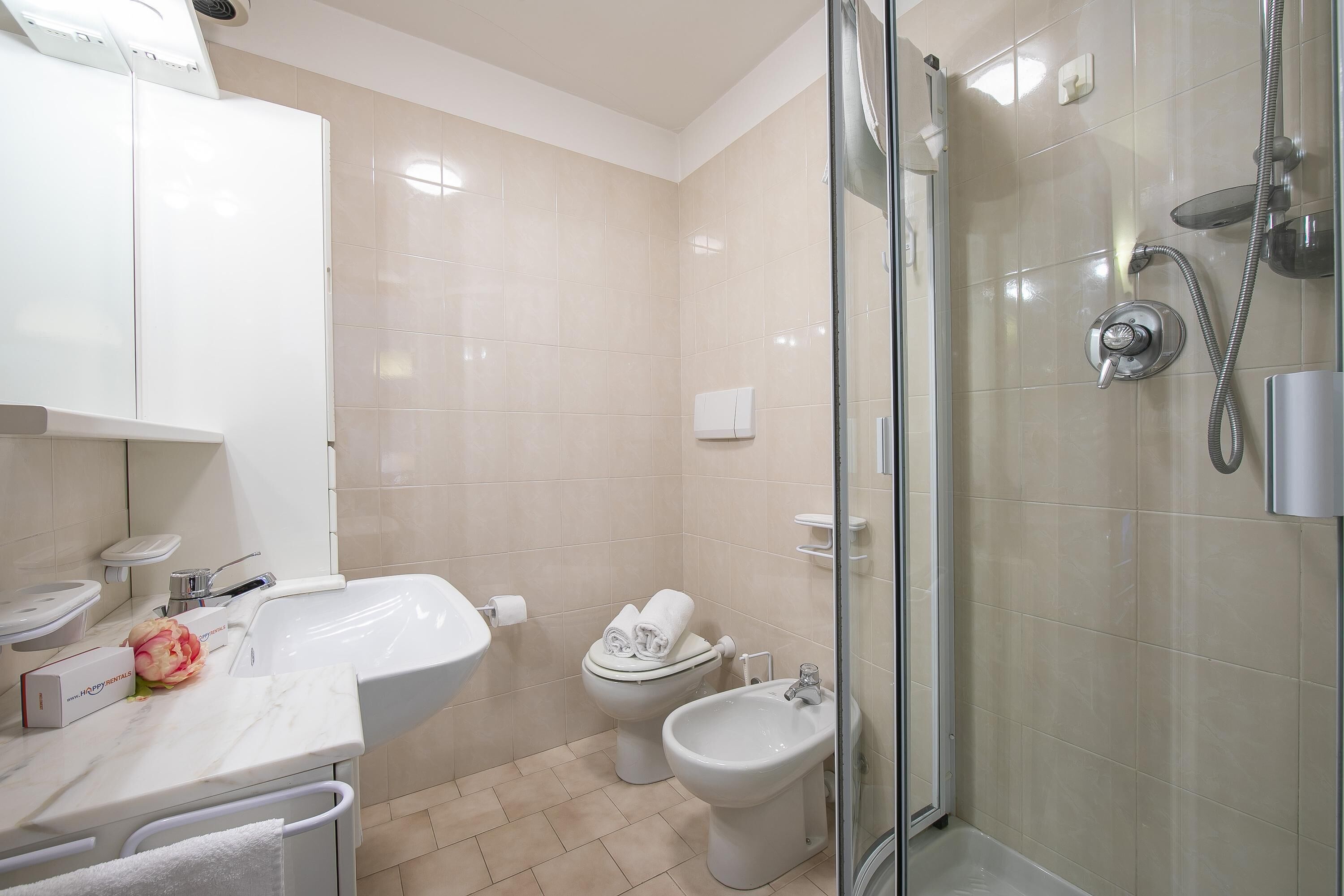 A modern bathroom with a sink, toilet, bidet, and glass-enclosed shower.