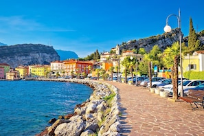 A coastal town with colorful buildings, a stone-paved promenade, and parked cars along the waterfront.