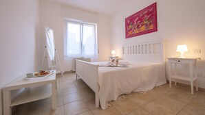 A bedroom with a bed, a bedside table with a lamp, a small table with a tray of breakfast, a window, and a radiator. - Casa Al Caprifoglio in Ispra (Ispra)