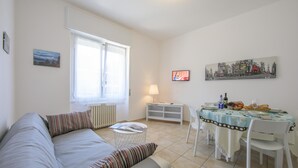 A living room with a sofa, a dining table with chairs, a lamp, and artwork on the walls. - Casa Al Caprifoglio in Ispra (Ispra)