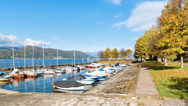 A marina with boats docked along a stone quay, a grassy path, and trees with autumn leaves. - Casa Al Caprifoglio in Ispra (Ispra)