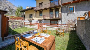 Un área de comedor al aire libre de madera, con una mesa preparada para dos personas, rodeada por un muro de piedra y una valla de madera.