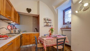 Una cocina con armarios de madera, una mesa de comedor dispuesta con platos y un florero, y una ventana con vistas al exterior.