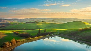 A serene landscape with rolling green hills, a calm lake reflecting the sky, and distant hills under a clear blue sky. - Maramaldo Morellino Shared Pool Chianti (Castelfiorentino)