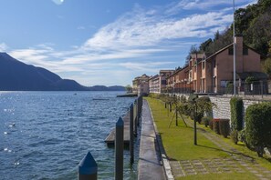 Una propiedad frente al agua con un sendero de piedra, setos cuidadosamente recortados y una hilera de edificios con balcones con vista al agua.