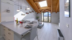 A modern kitchen with a dining area, wooden ceiling beams, and a view of the outdoors. - Blu Lake Apartment on Ghiffa Beach (Ghiffa)