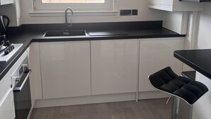 A modern kitchen with white cabinets, a black countertop, a sink, and a window. - 2 Bed Flat - Sleeps 4 - Pets - Parking - Wifi (Edinburgh)