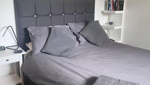 A neatly made bed with grey bedding and pillows, a bedside table with a lamp, a small shelf with books, and a wall clock. - 2 Bed Flat - Sleeps 4 - Pets - Parking - Wifi (Edinburgh)