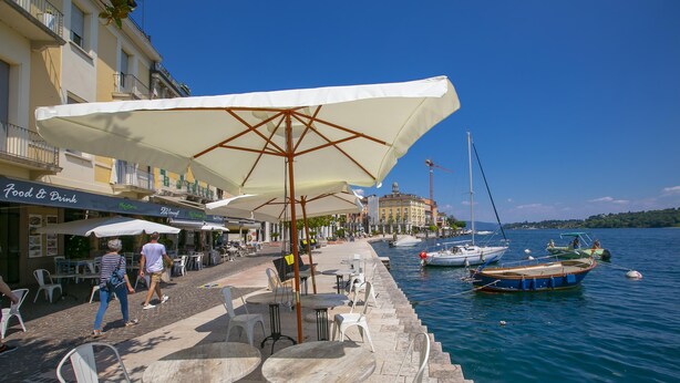 Ein Café direkt am Wasser mit Außenbereich, Tischen und Sonnenschirmen mit Blick auf ein Gewässer und Boote.