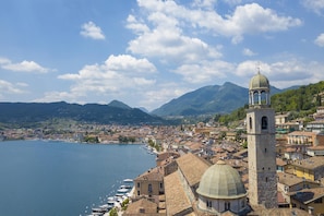 A coastal town with a prominent tower and a large dome, surrounded by water and mountains. - Casa Mirabella With Lake View (Salò)