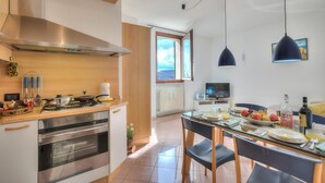 Eine moderne Küche mit Edelstahlgeräten, ein Essbereich mit einem Glastisch und Meerblick durch ein großes Fenster.