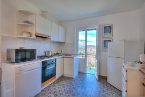 Eine kleine Küche mit weißen Schränken, einer Mikrowelle, einem Herd, einem Backofen und einem Kühlschrank.