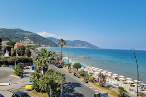 A coastal road with parked cars, palm trees, and beach umbrellas. - Laigueglia Beach in Laigueglia (Laigueglia)