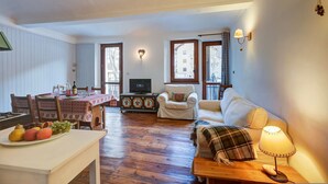 A cozy living room with a wooden floor, a white sofa, a dining table with chairs, and a television. - Appartamento Zia Anna Ski in Ski out (Sauze d'Oulx)