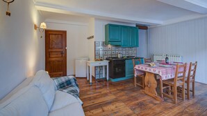 A compact kitchen with teal cabinets, a small table, and a dining area with a checkered tablecloth. - Appartamento Zia Anna Ski in Ski out (Sauze d'Oulx)