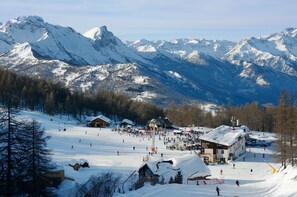 Une station de ski avec un grand bâtiment, des pistes de ski et des montagnes enneigées en arrière-plan.