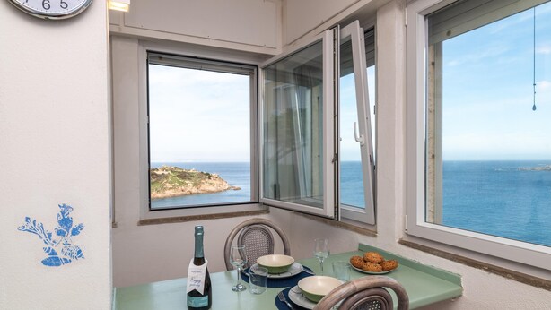 Ein Essbereich mit einem Tisch für zwei Personen, einer Weinflasche und Blick aufs Meer.