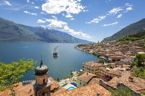 A coastal town with a church, a boat on the water, and mountains in the background. - Il Nido Dell Artista (Tenno)