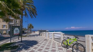 Une promenade dallée, avec des vélos, des palmiers et une vue sur la mer.
