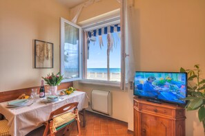 A dining area with a table set for two, a television, and a window with a view of the sea. - Mer Vivante - Front Beach (Albenga)