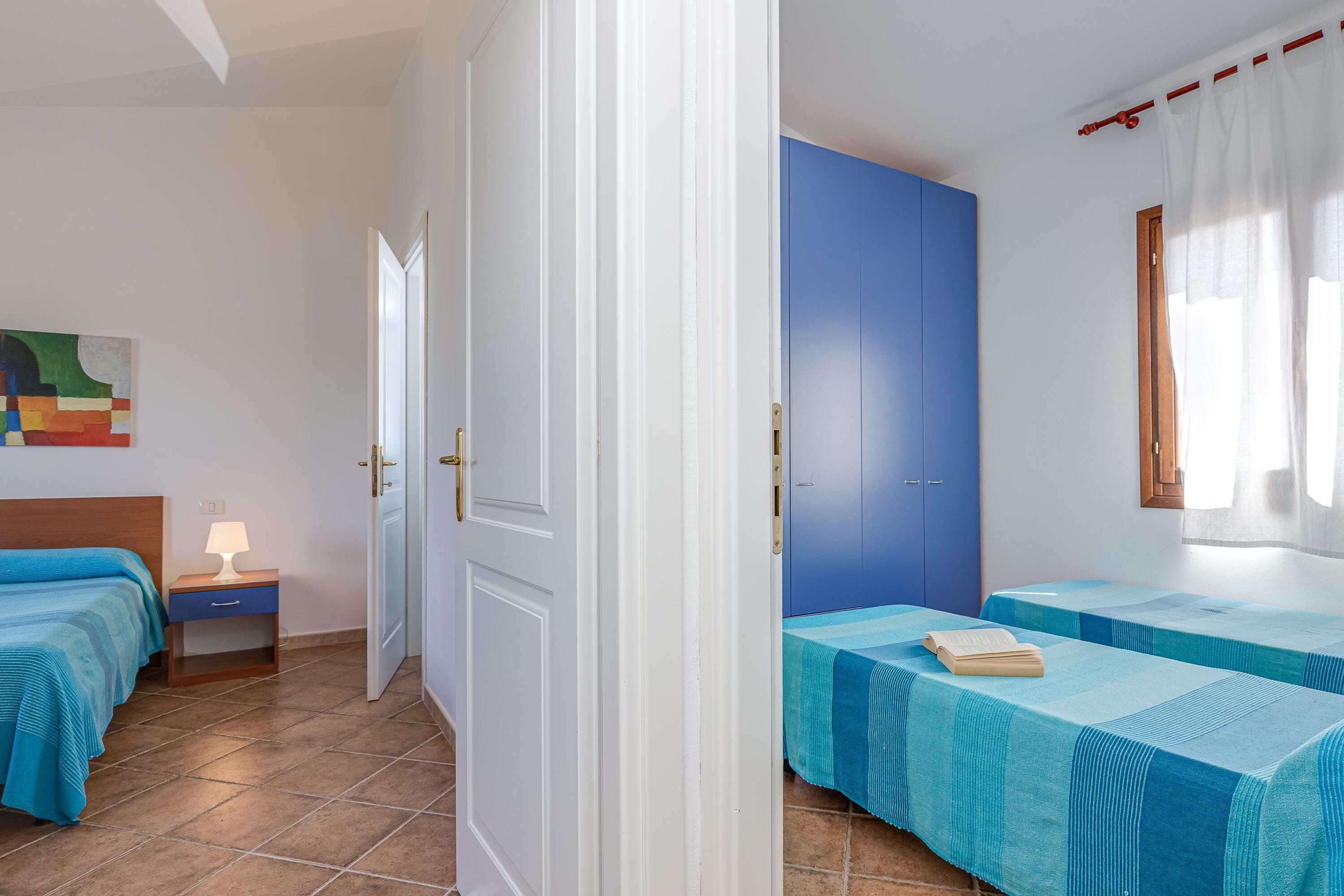Ein Zimmer mit zwei Betten, einem Nachttisch, einem Bild und einem fenster mit Vorhängen.