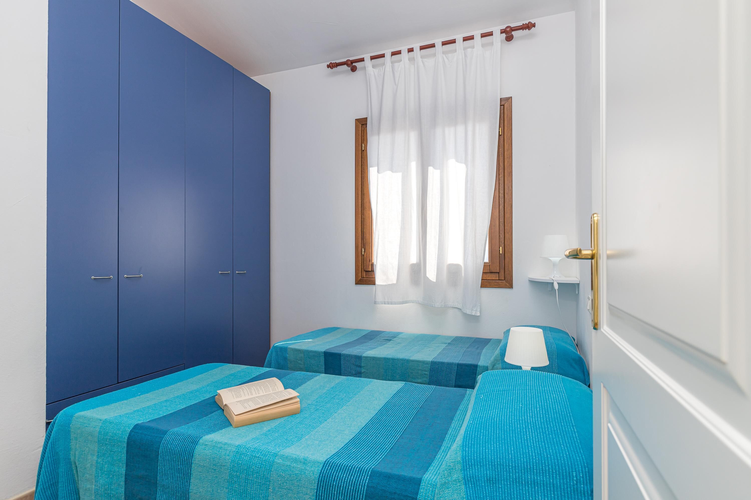 A room with two beds, a wardrobe, and a window with curtains.