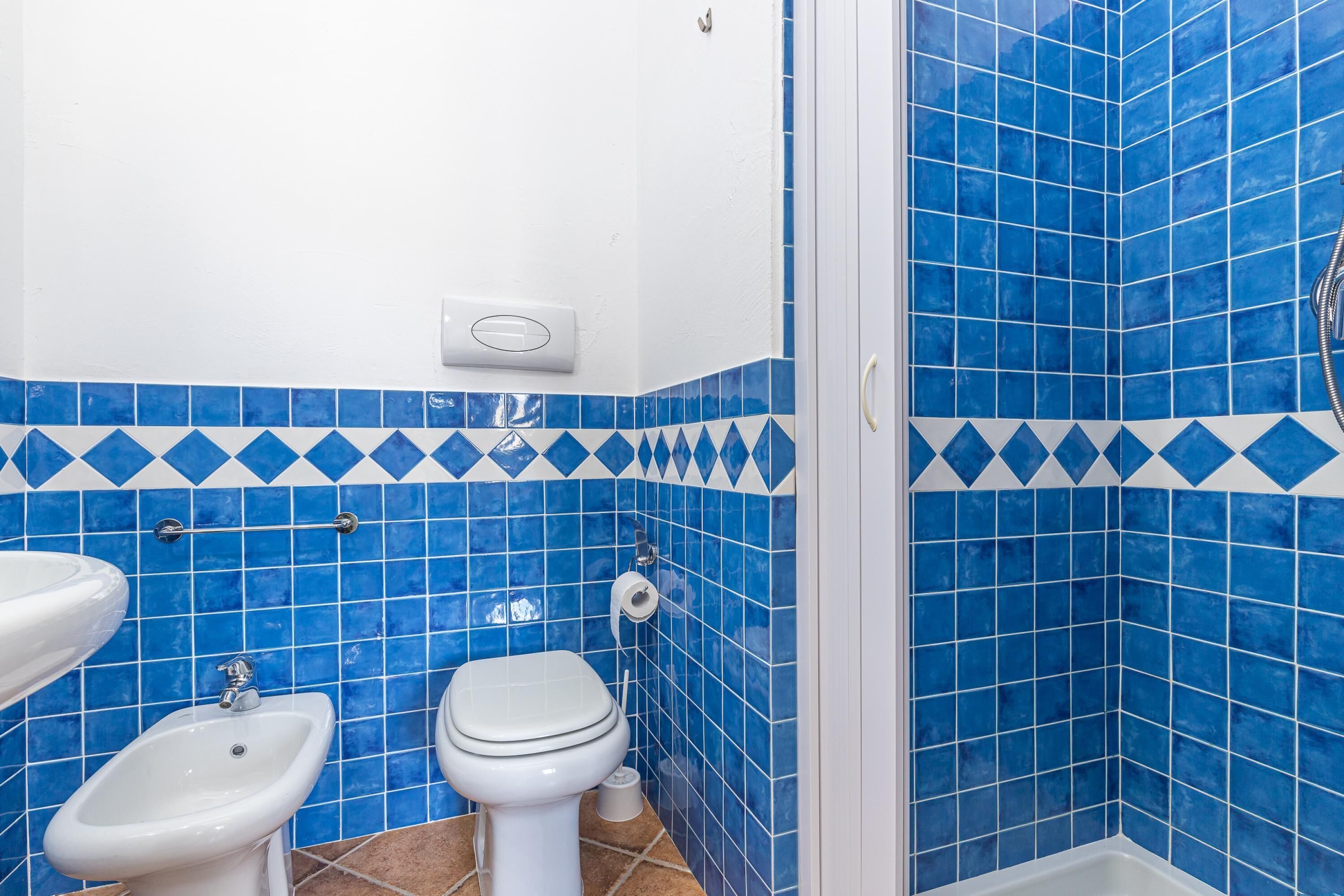 A bathroom with blue-tiled walls, a white sink, a bidet, and a toilet.