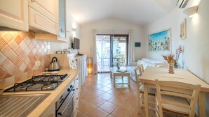 A kitchen with a gas stove, oven, and a kettle. There is a dining area with a table and chairs. - Dimora di Rosy Pittulongu (Olbia)