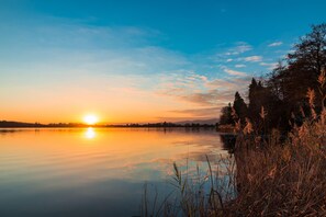 Ein ruhiger See bei Sonnenuntergang, mit klarem Himmel und Bäumen am Ufer.