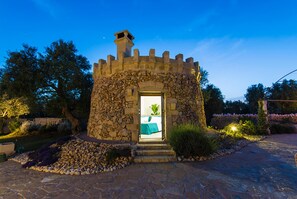 Un bâtiment en pierre avec une porte d’entrée donnant sur une pièce où se trouvent un lit et une plante.